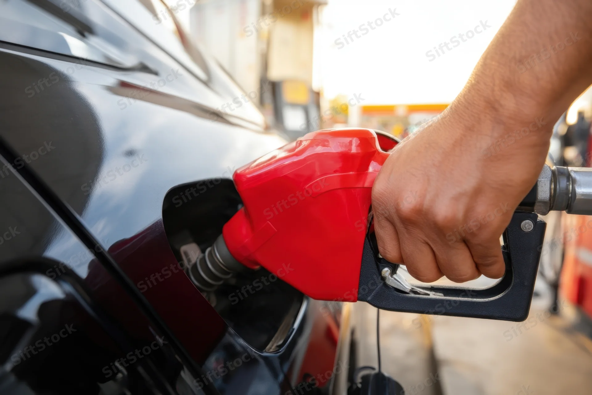 Hand holding red fuel nozzle inserting into car tank at gas station