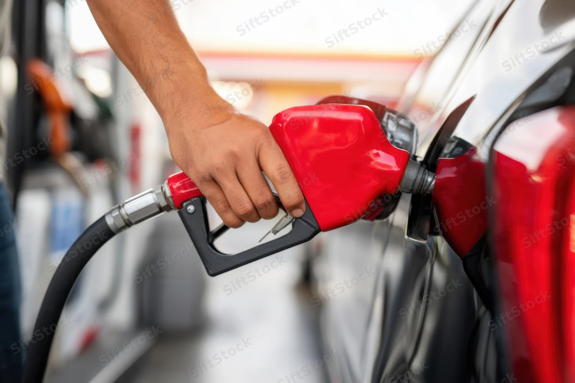 Hand holding red fuel nozzle inserted into car tank at gas station
