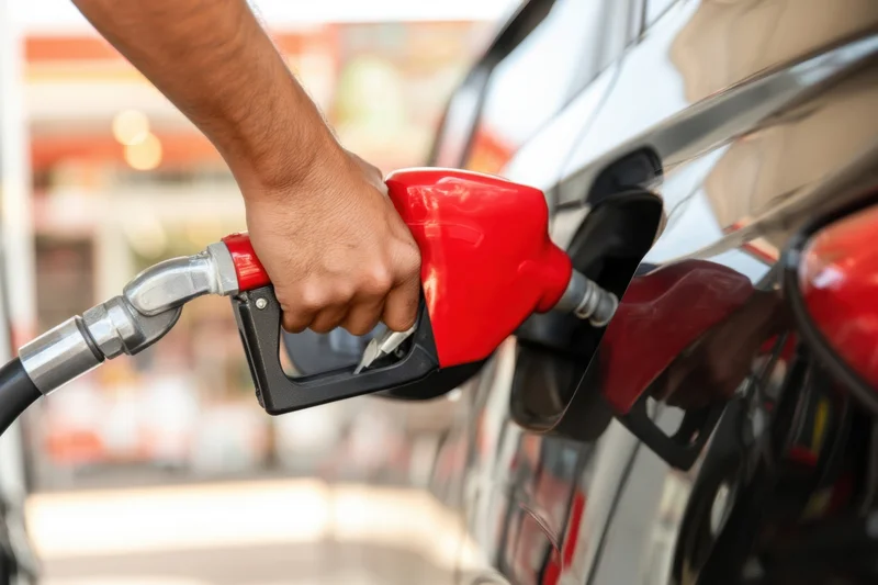 Hand gripping red fuel pump nozzle inserted into car tank at gas station