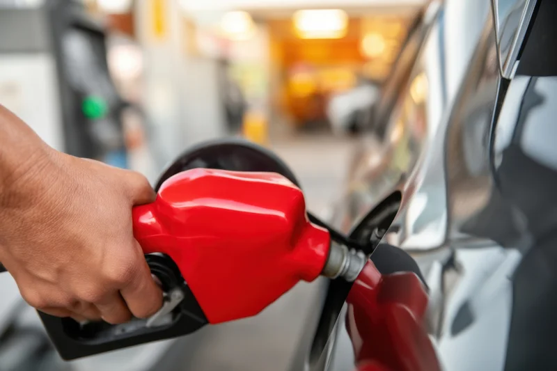 Hand holding red fuel pump nozzle inserted into car tank at gas station