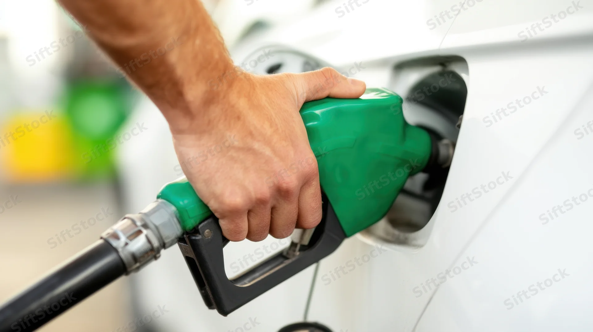 Hand holding green fuel pump nozzle inserted into car tank at gas station