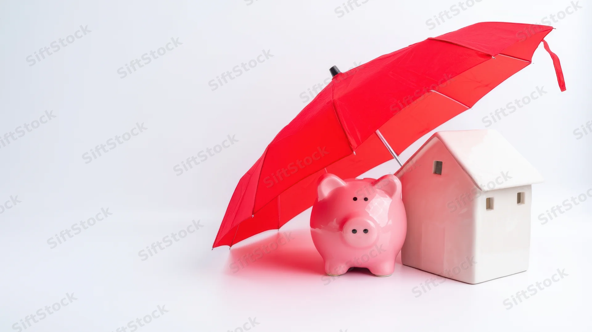 Pink piggybank and white house model under red umbrella on white background
