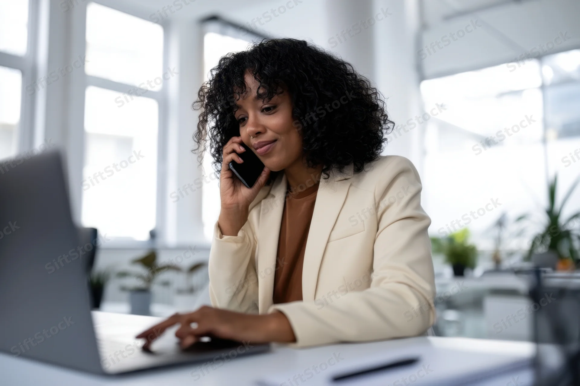 Woman talking on phone while typing on laptop at office desk