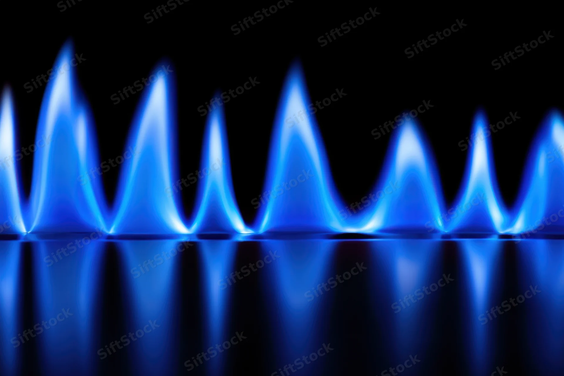 Row of blue flames burning on a gas stove burner with reflection on dark surface