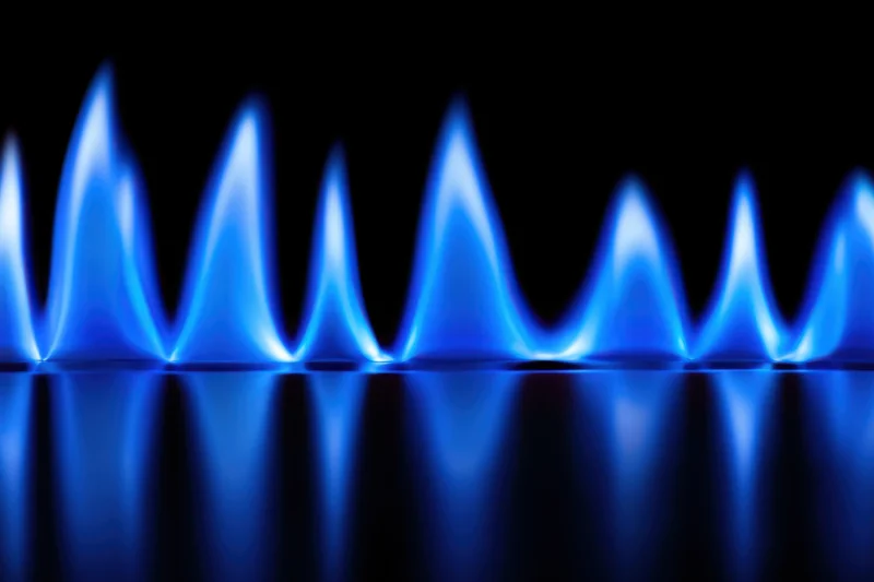 Row of blue flames burning on a gas stove burner with reflection on dark surface