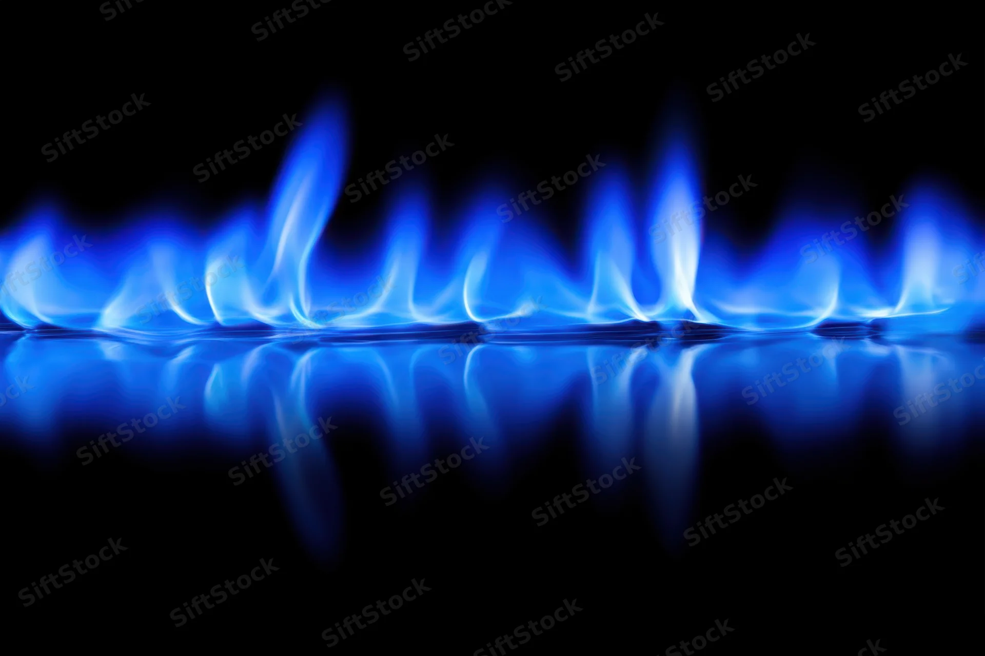 Blue flames burning on a gas stove burner with reflection on dark surface