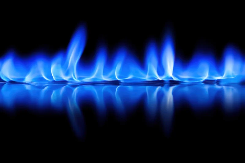Blue flames burning on a gas stove burner with reflection on dark surface