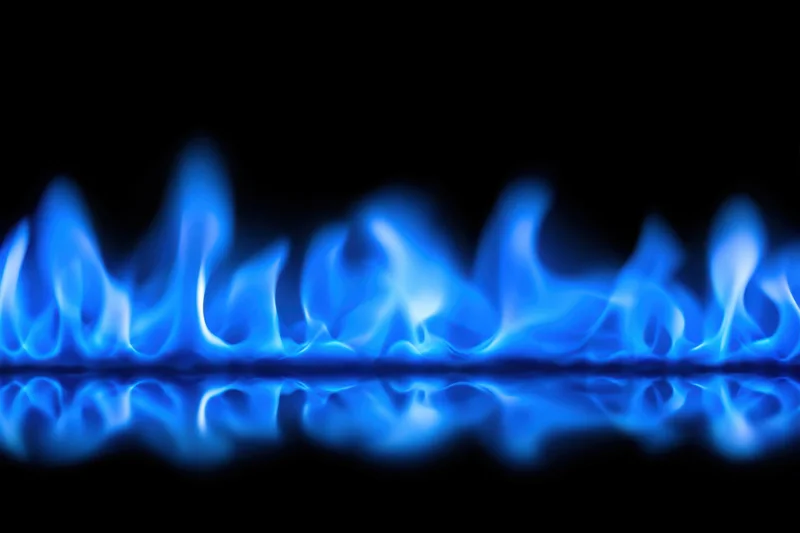 Blue flames burning along a reflective surface against a black background