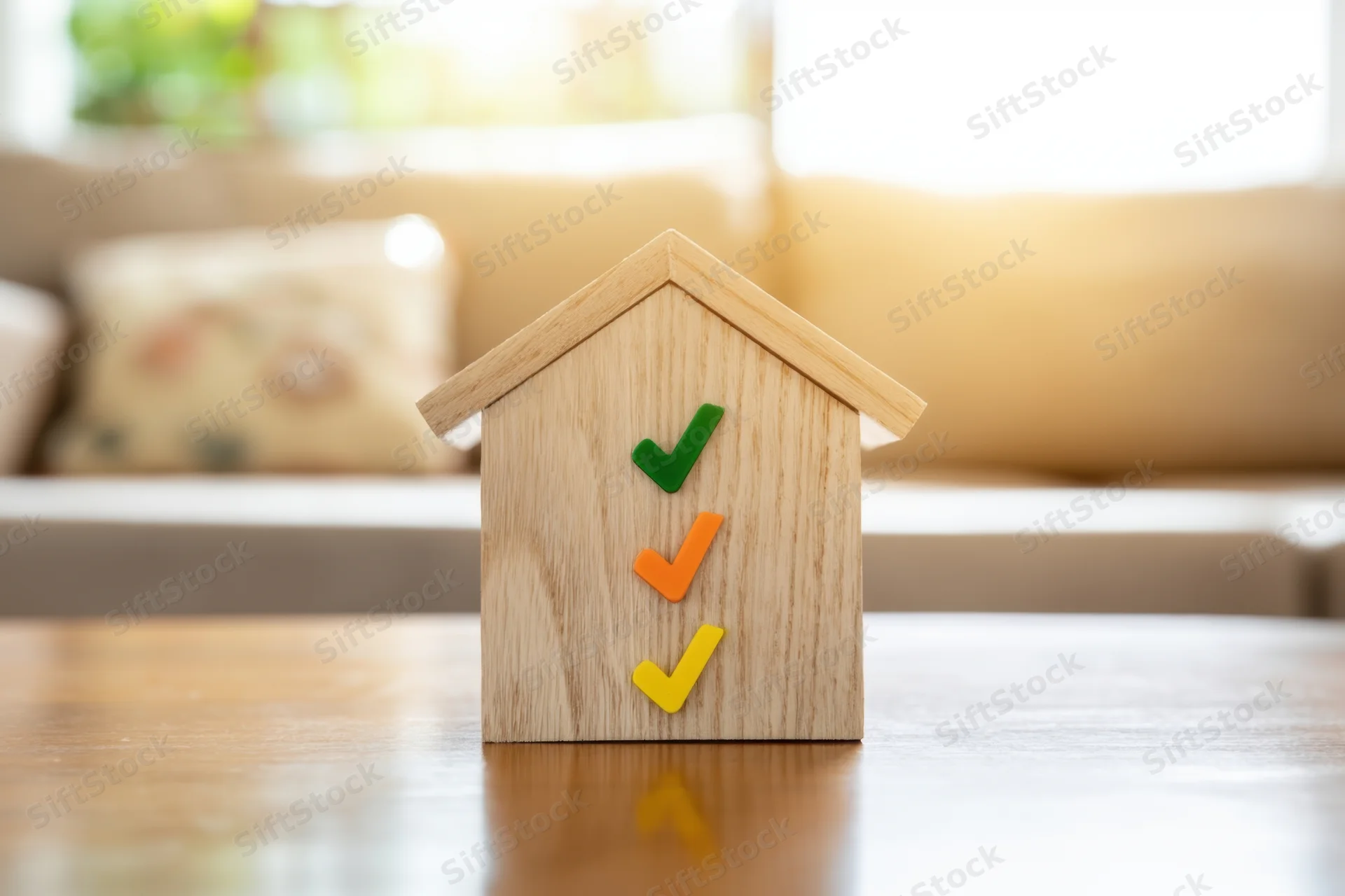 Wooden house model with colored checkmarks on a table in a living room