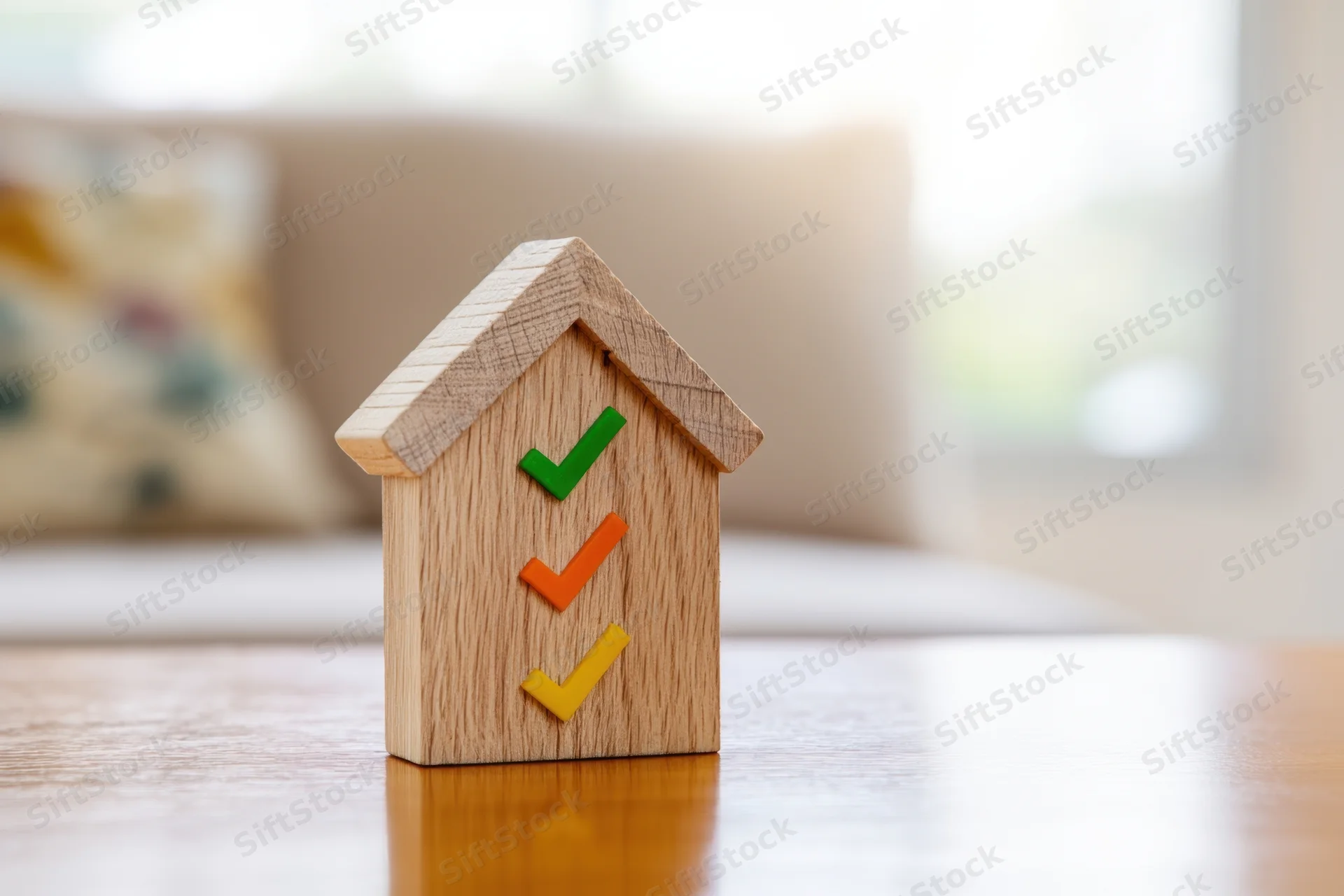 Wooden house model with colorful checkmarks on a table in a living room