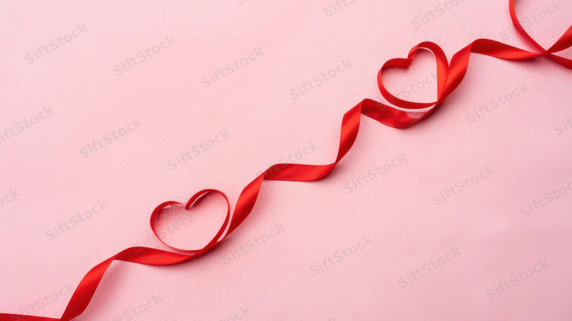 Red ribbon shaped into hearts on a soft pink surface