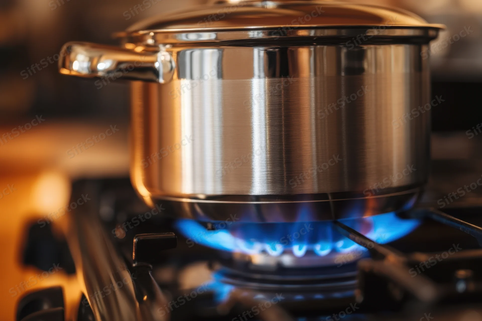 Stainless steel pot on gas stove burner with blue flame in kitchen