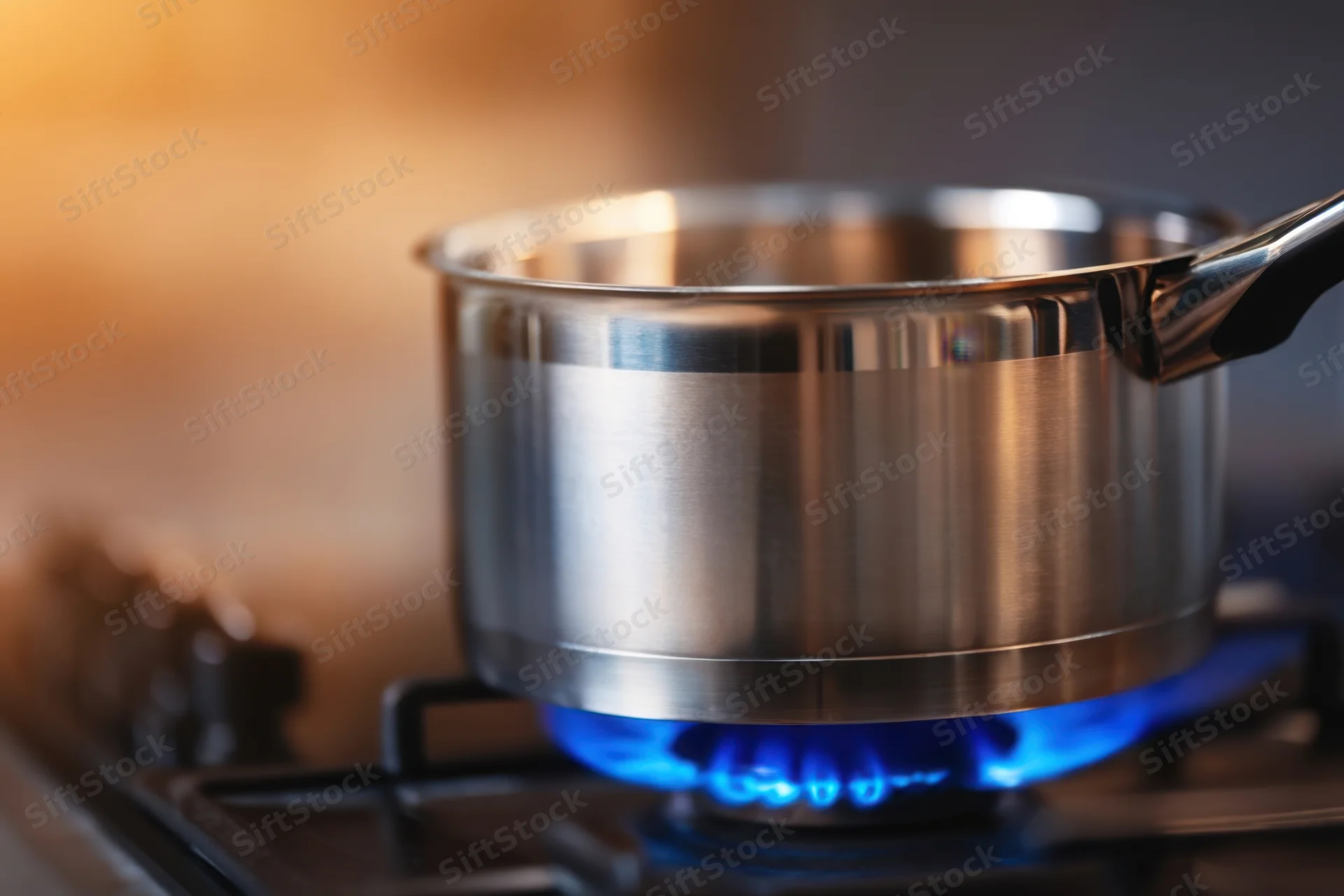 Stainless steel pot on gas stove with blue flame burning underneath in kitchen setting