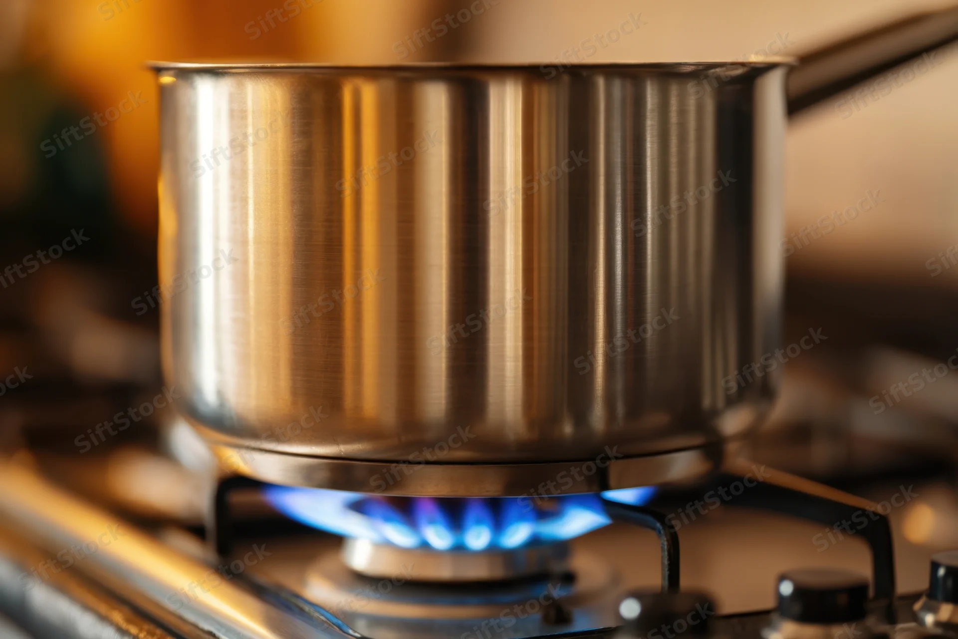 Stainless steel pot on gas stove burner with blue flame in kitchen
