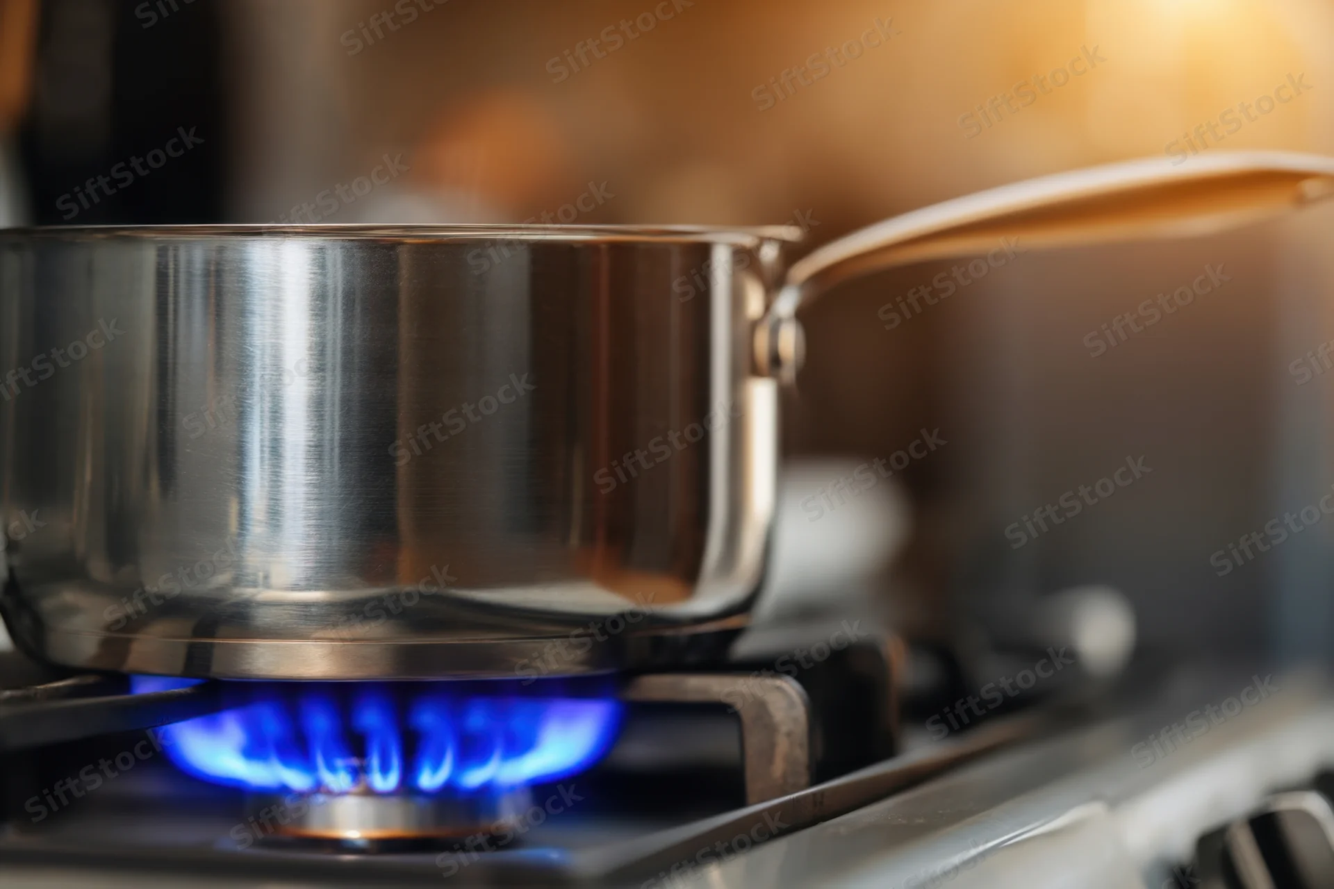 Stainless steel pot on a gas stove burner with blue flame in a kitchen