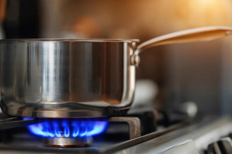 Stainless steel pot on a gas stove burner with blue flame in a kitchen