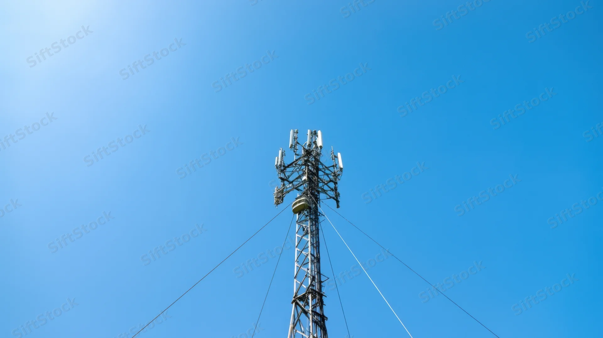 Low-angle view of a telecommunications tower with antennas against a clear blue sky