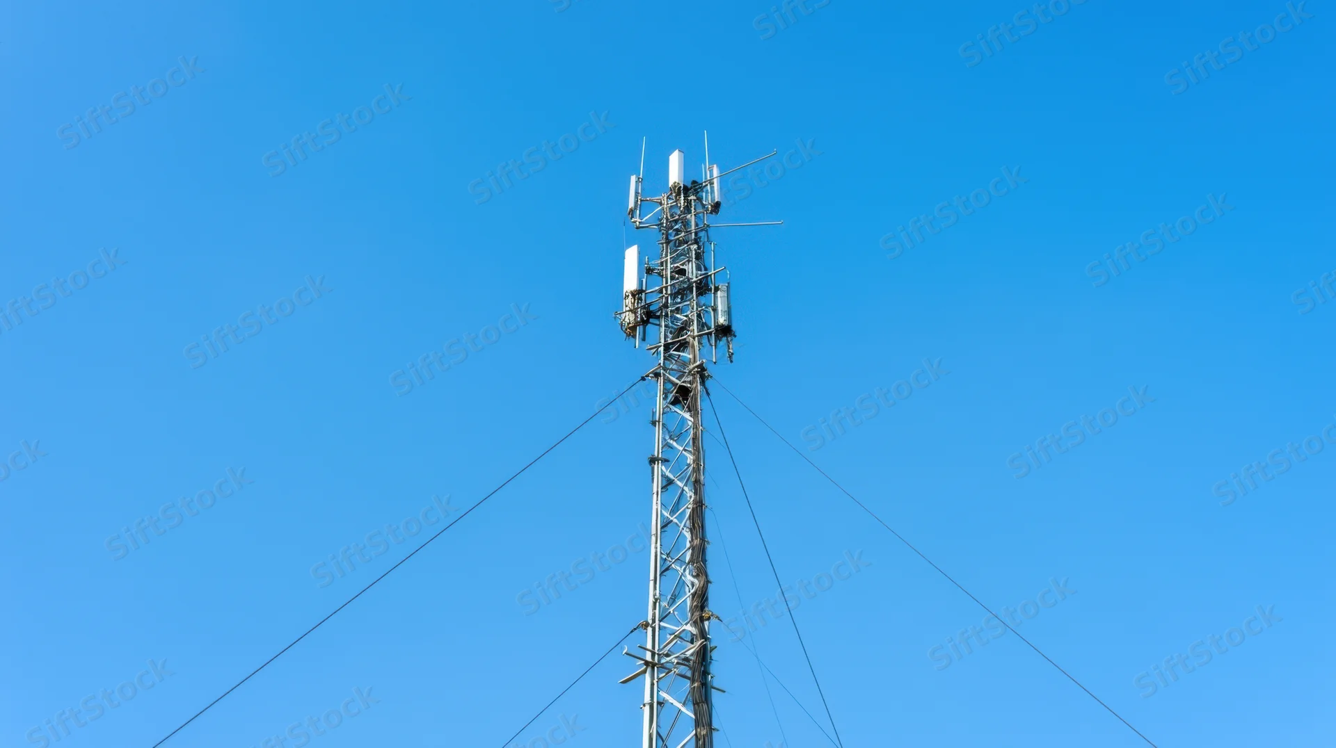 Tall metal communication tower with antennas and cables against a clear blue sky