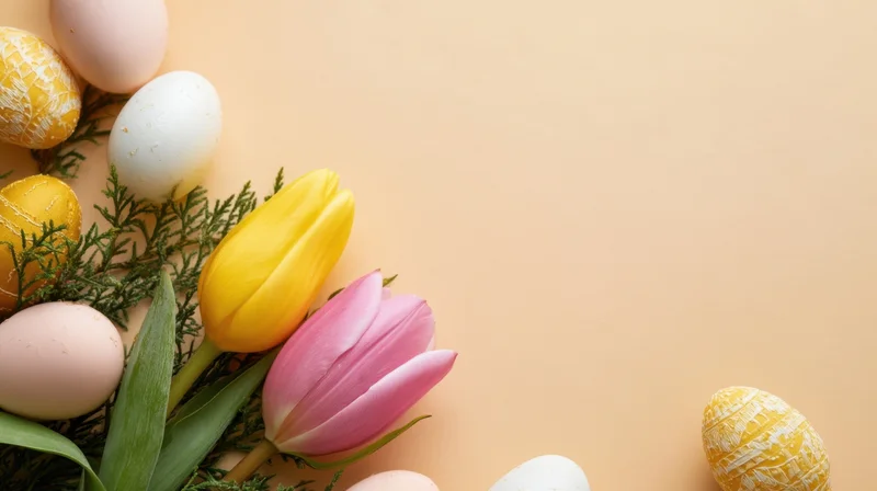 Easter eggs and tulips arranged with greenery on a peach surface with copyspace