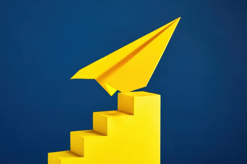 Yellow paper airplane launching from top of yellow steps against blue background