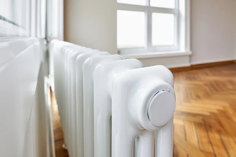White vintage-style radiator with control valve in a bright room with wooden parquet floor and window