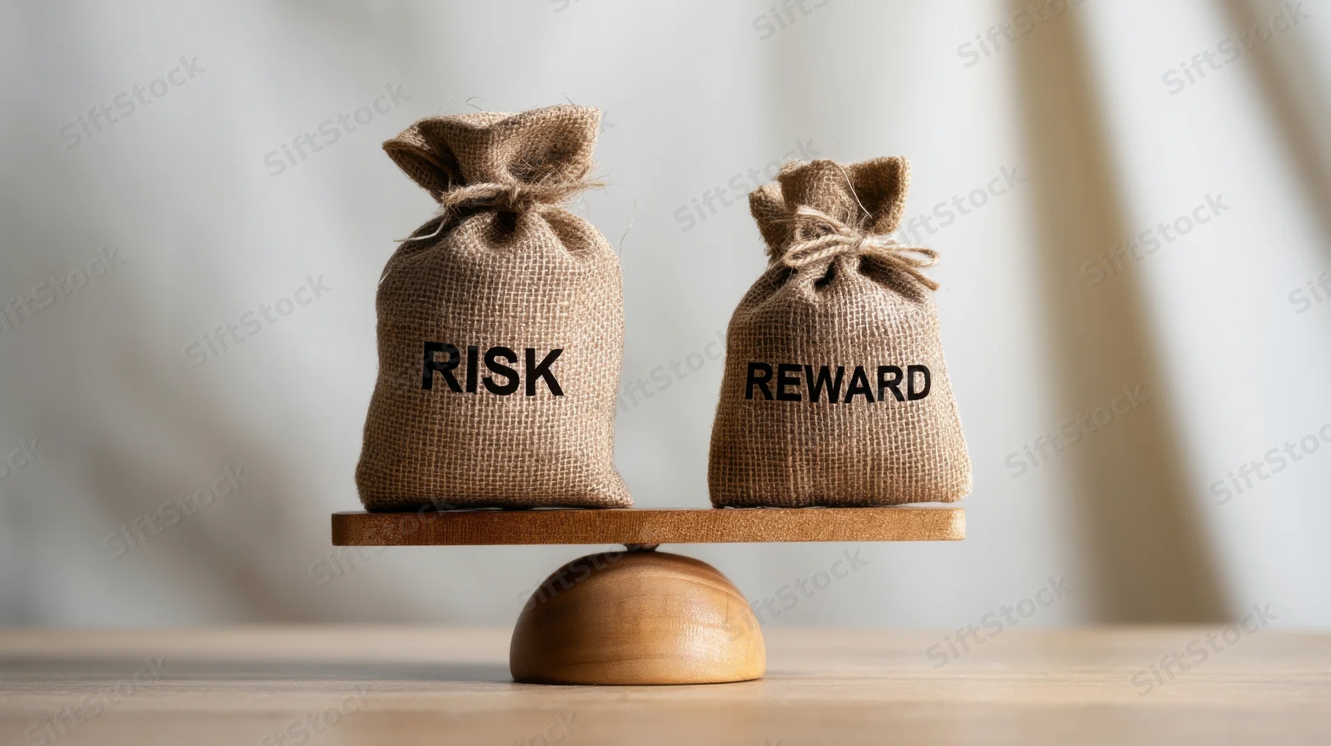Two burlap bags labeled risk and reward balanced on a wooden scale on a table