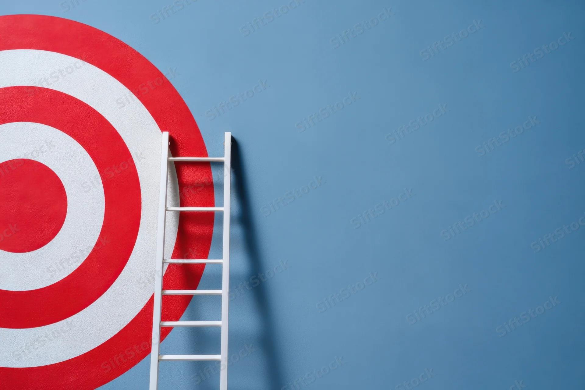 White ladder leaning against a red and white target on a blue wall