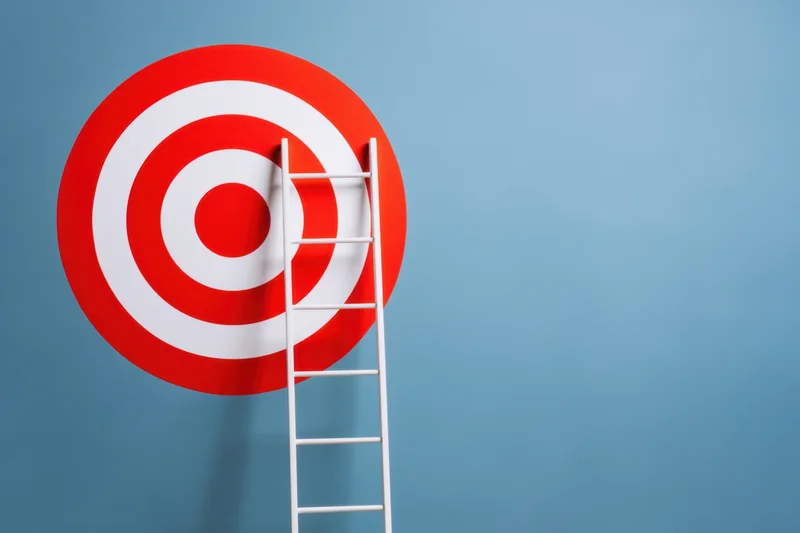 White ladder leaning against red and white target on blue background