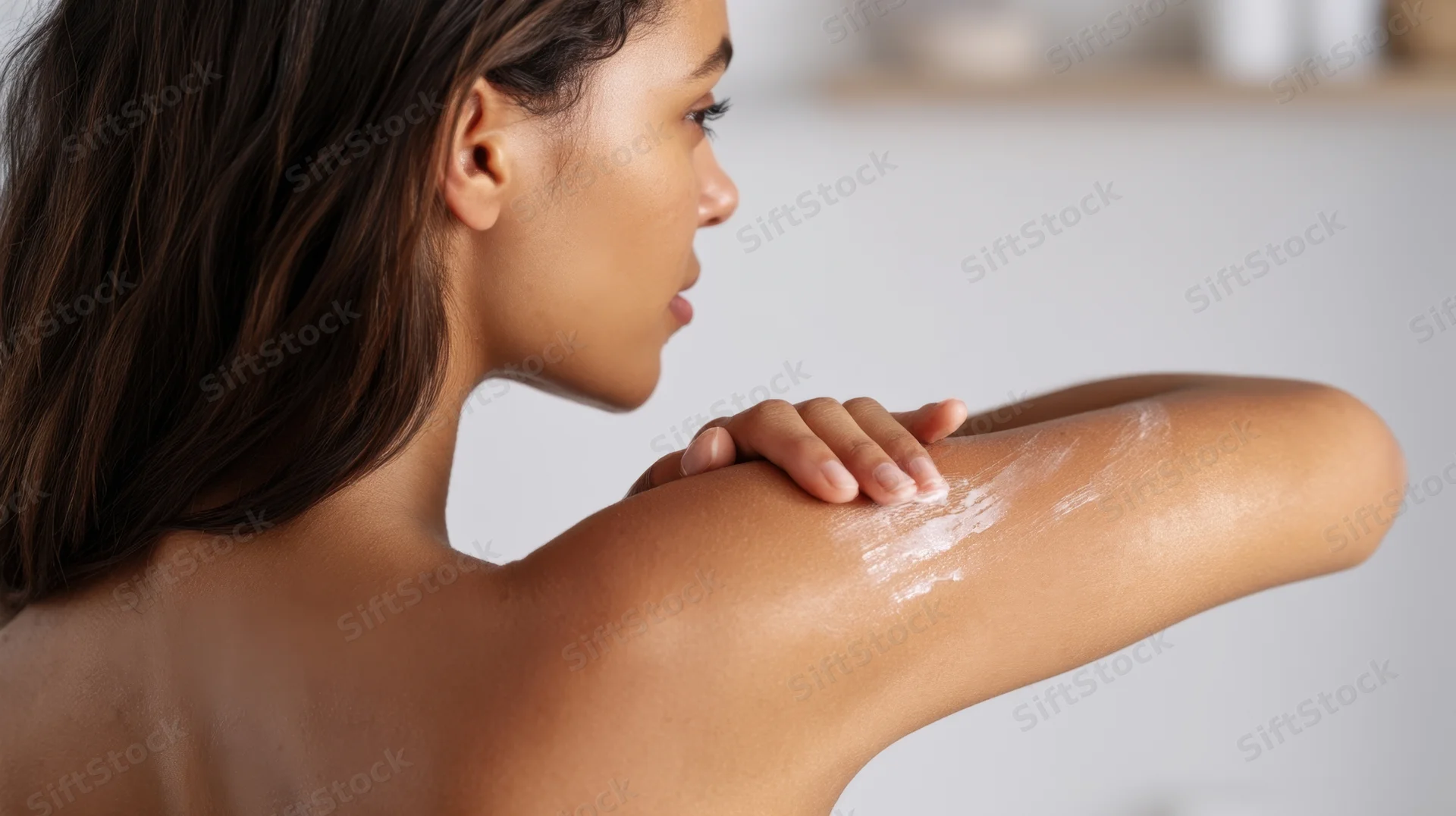 Woman applying moisturizer to her shoulder in a bathroom setting