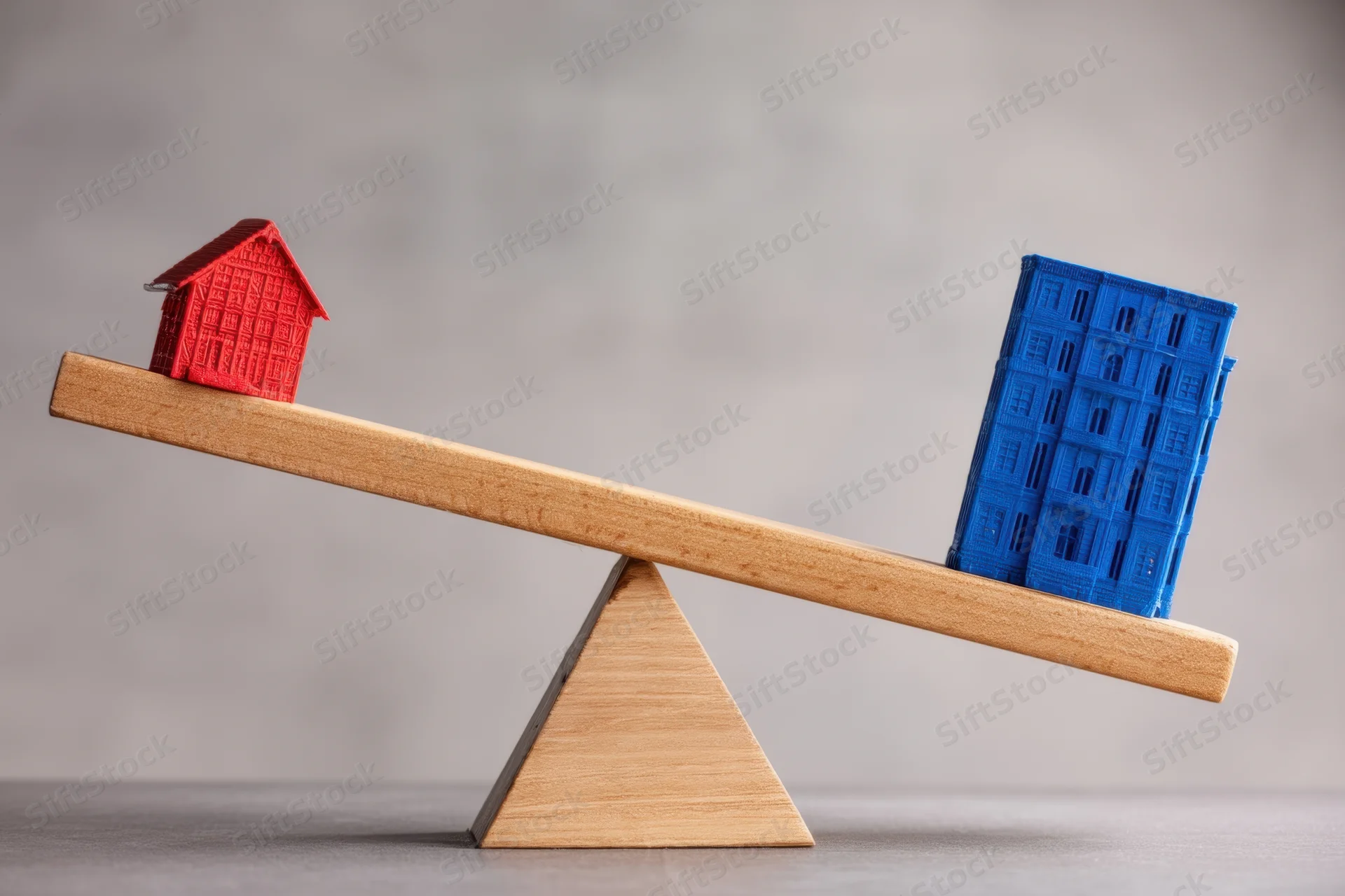 Red house and blue apartment building on a wooden seesaw balanced on a triangular fulcrum