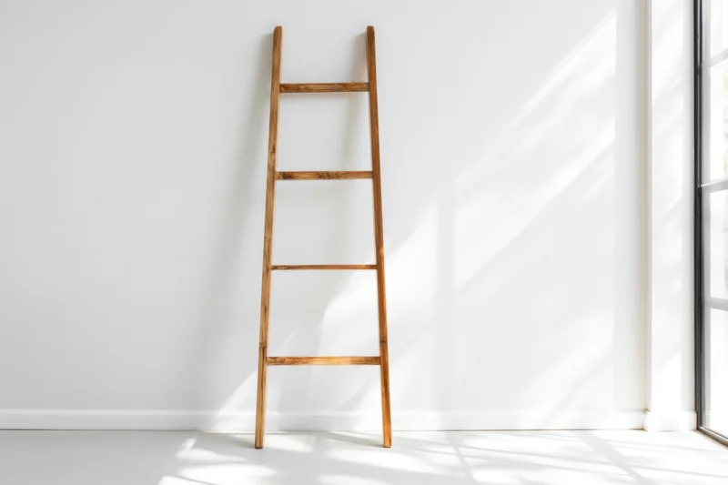 Wooden ladder leaning against white wall in bright minimalist room with sunlight and shadows from window