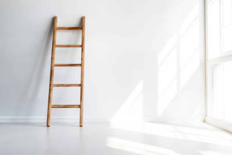 Wooden ladder leaning against white wall in bright minimalist room with sunlight streaming through window
