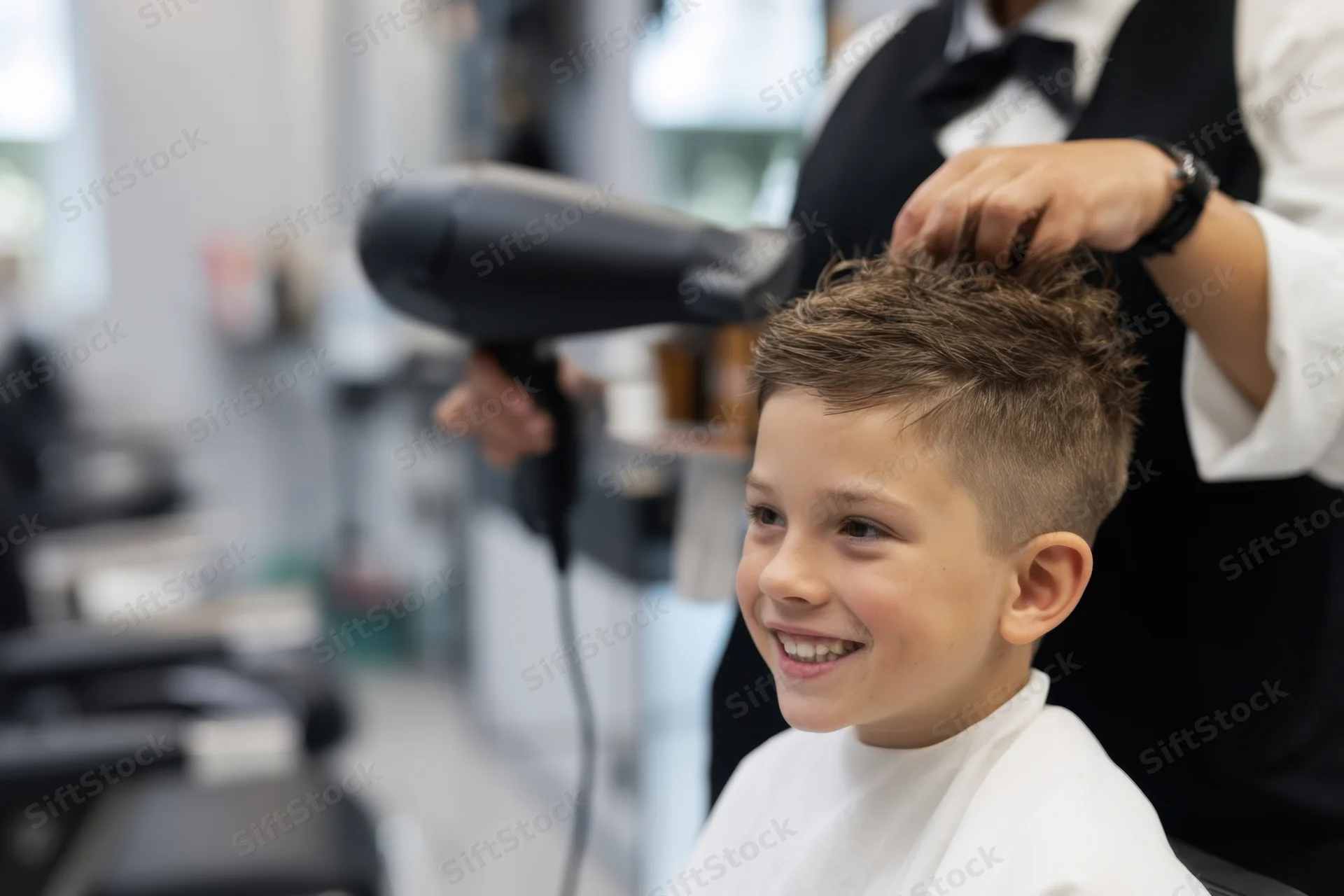 Young boy smiling while getting his hair styled with a hairdryer in a salon