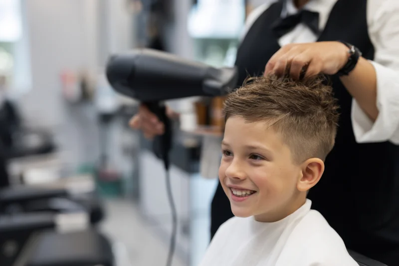 Young boy smiling while getting his hair styled with a hairdryer in a salon