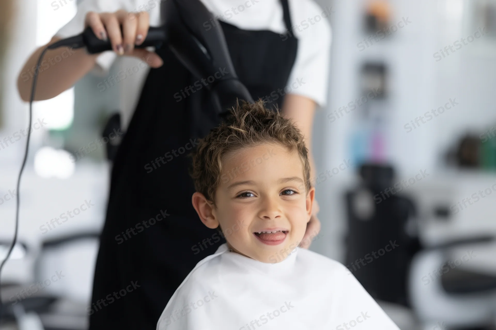 Young boy smiling while a stylist blow-dries his hair in a salon
