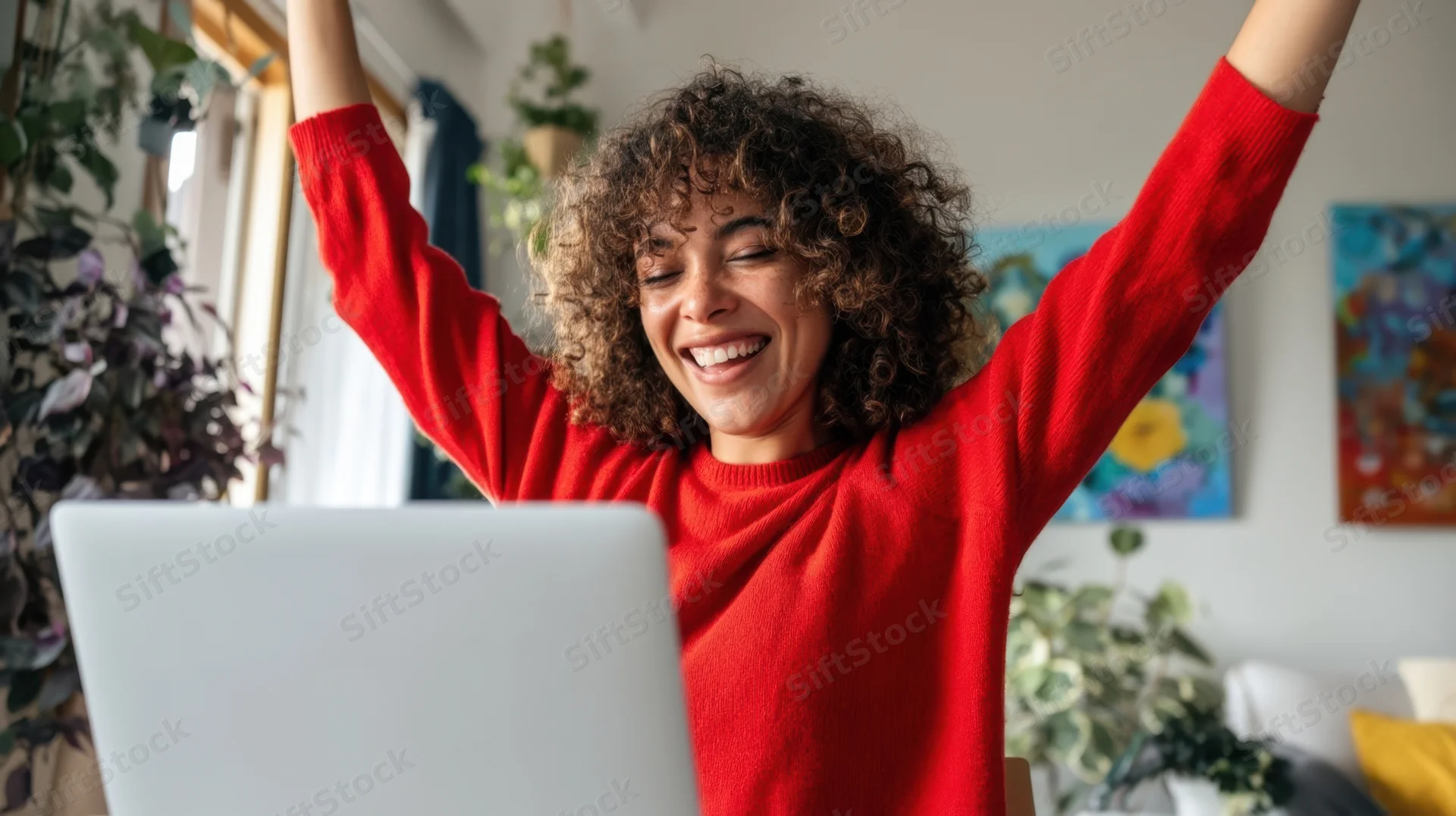 Young woman celebrating with arms raised in front of laptop at home office