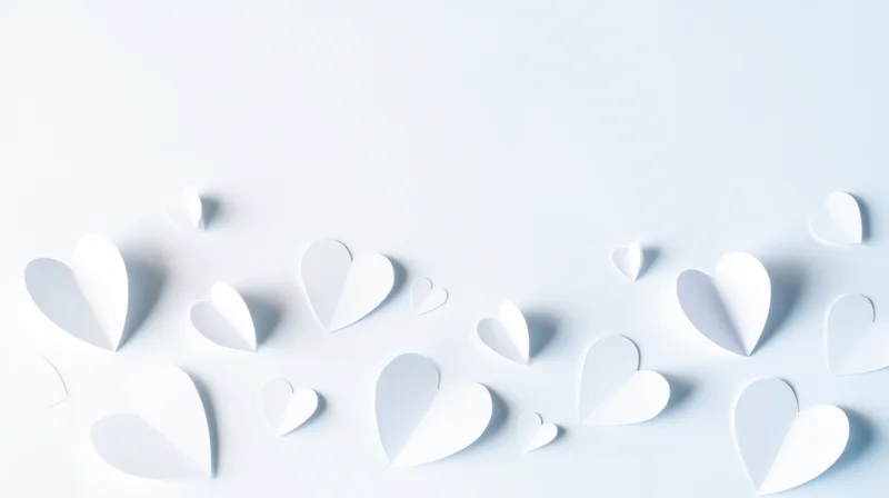 White paper hearts arranged on a light surface with copyspace