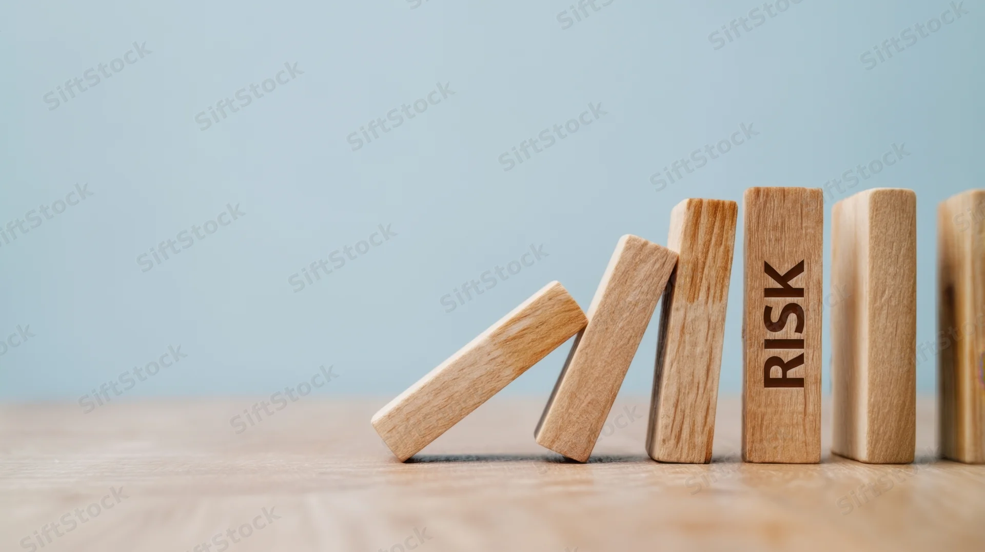 Wooden dominoes falling in a chain reaction with one labeled risk on a light blue background