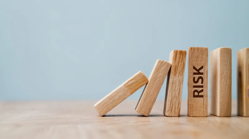 Wooden dominoes falling in a chain reaction with one labeled risk on a light blue background