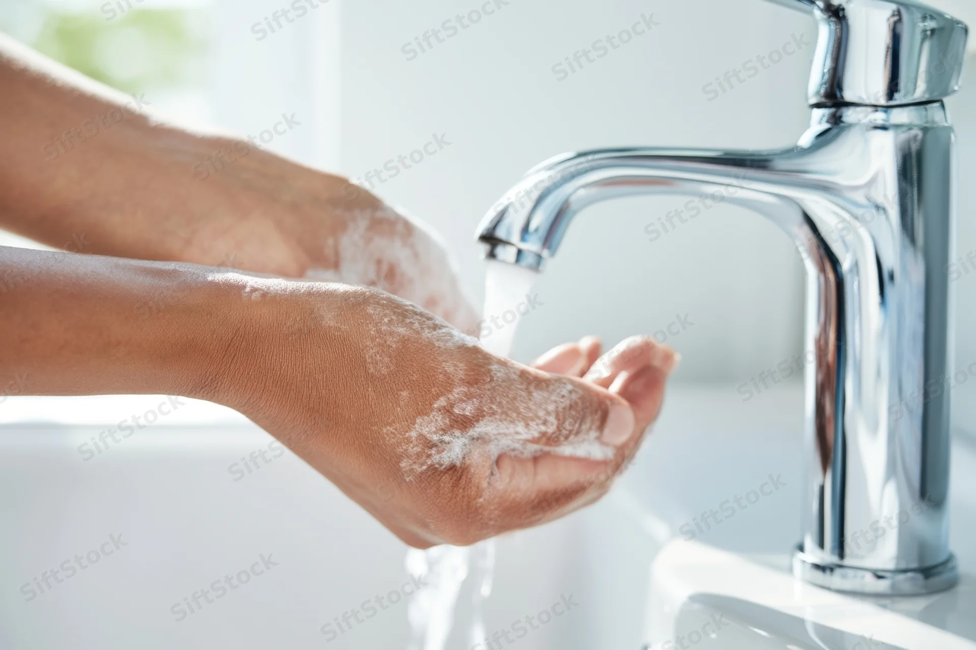 Hands covered in soap lather under running water from a chrome faucet in a bathroom sink