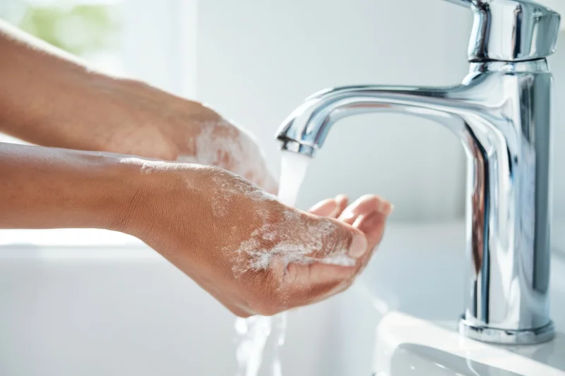 Hands covered in soap lather under running water from a chrome faucet in a bathroom sink