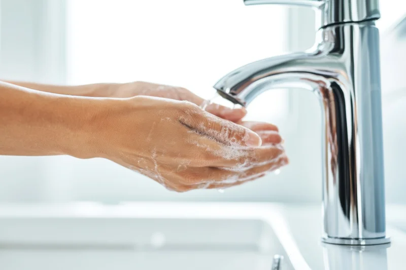 Hands being washed with soap under running water at a chrome faucet in a bathroom sink
