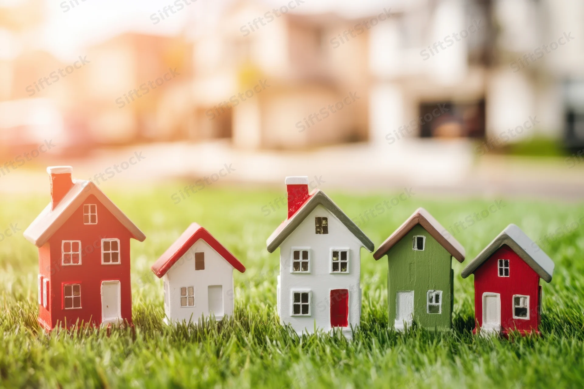 Miniature houses arranged in a row on a grassy lawn with a blurred residential background