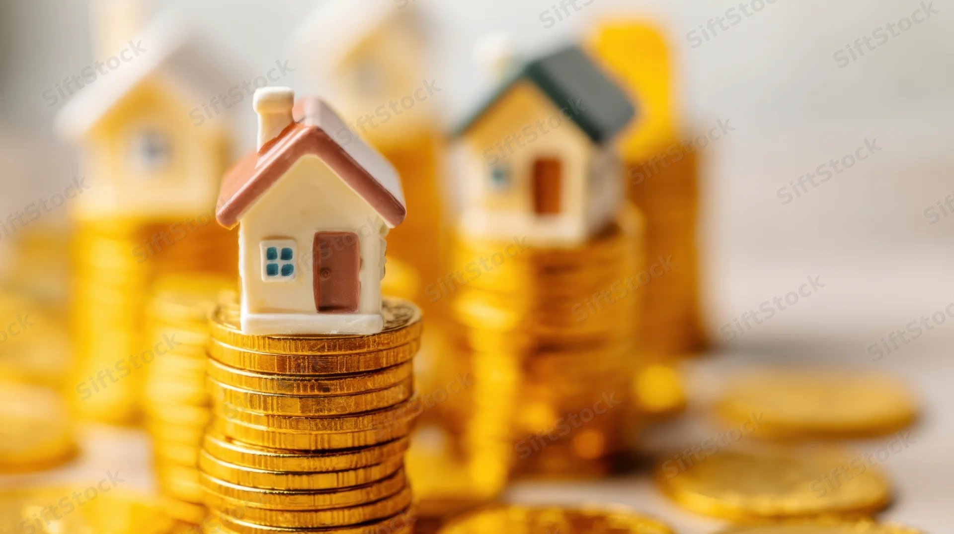Miniature houses stacked on golden coins representing real estate investment