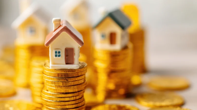 Miniature houses stacked on golden coins representing real estate investment