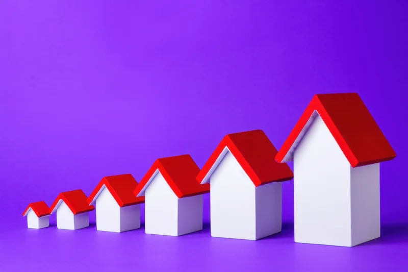 Row of miniature white houses with red roofs increasing in size from left to right on purple background