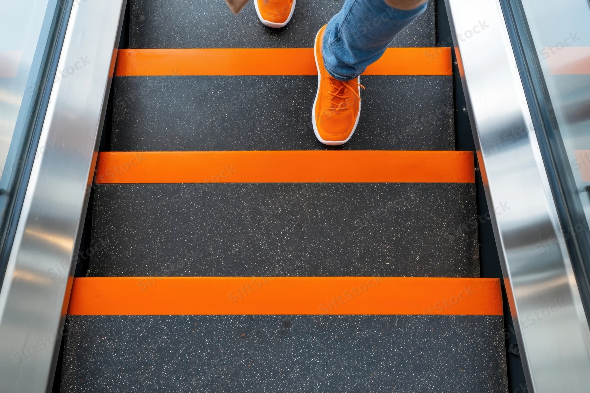 Person ascending escalator in orange sneakers and jeans, viewed from above