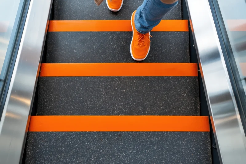 Person ascending escalator in orange sneakers and jeans, viewed from above