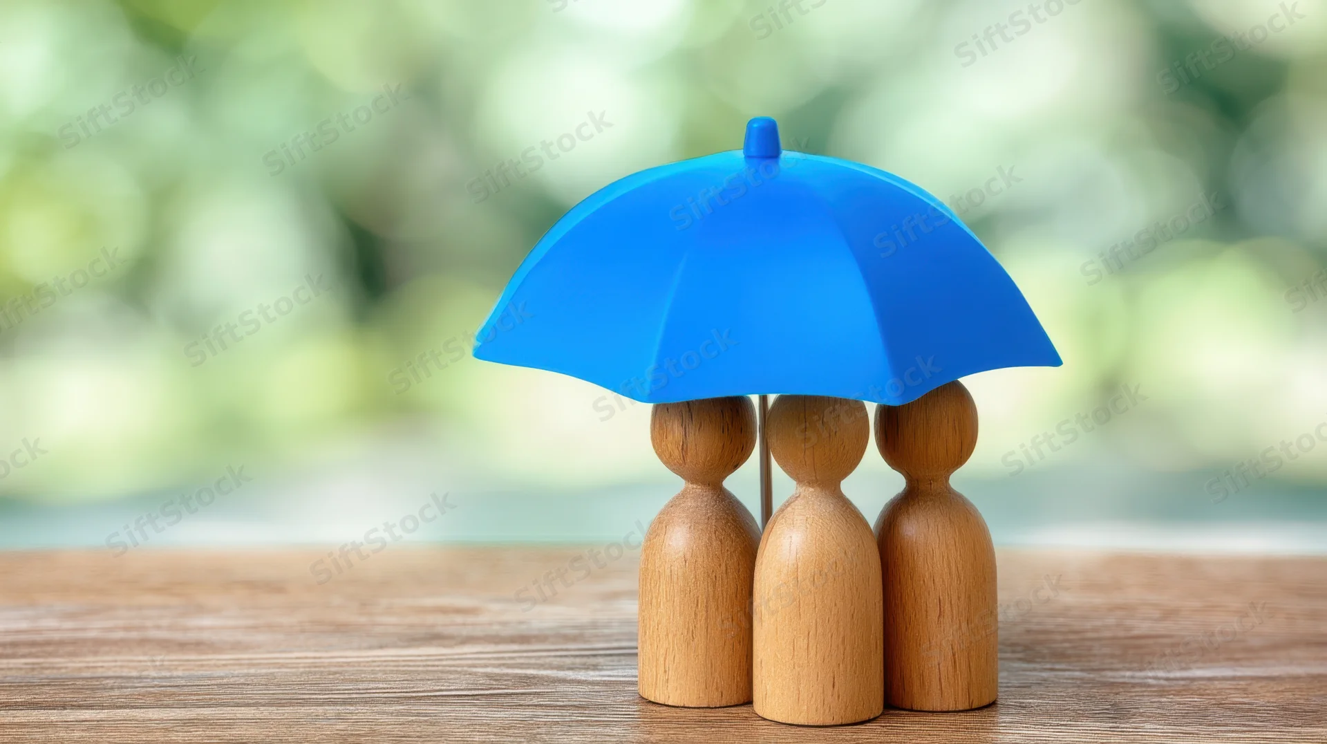 Three wooden figurines under a blue umbrella on a wooden table