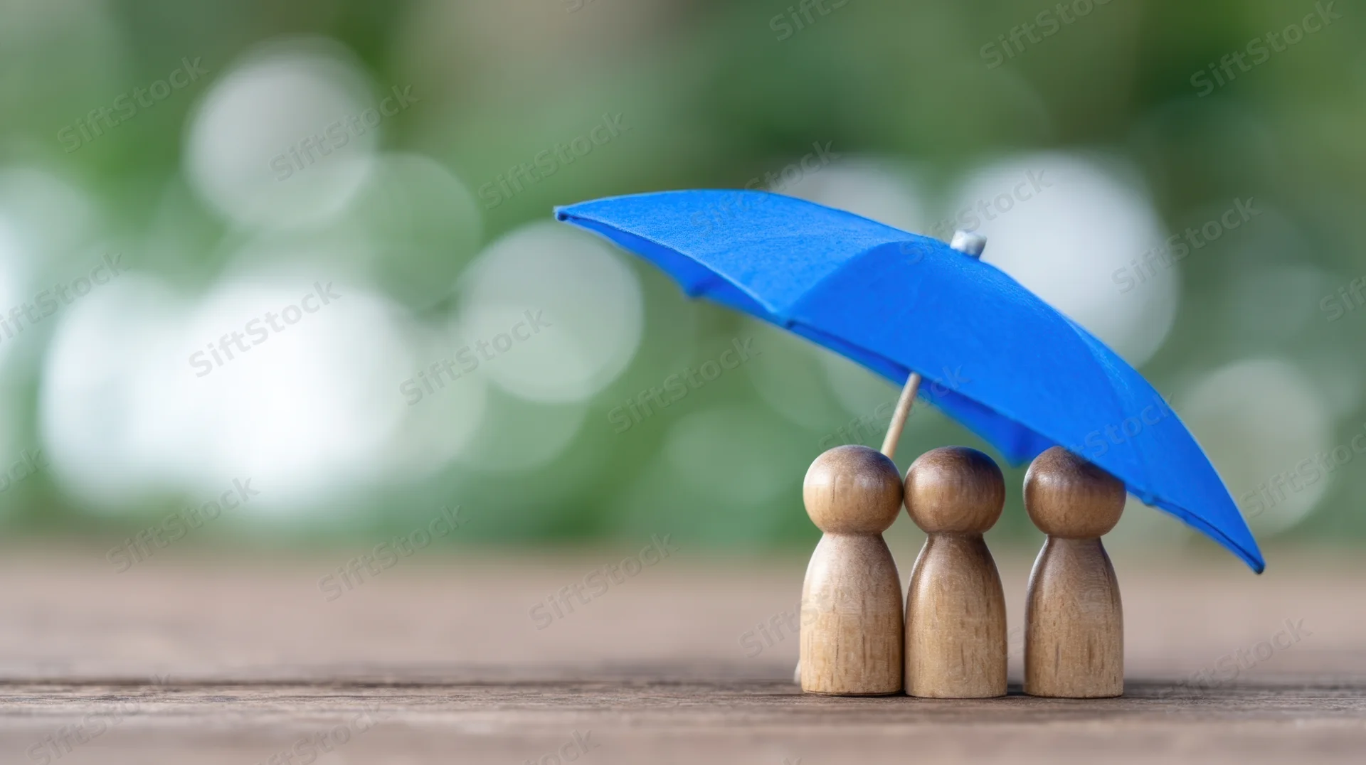 Three wooden figures under a blue umbrella on a wooden surface